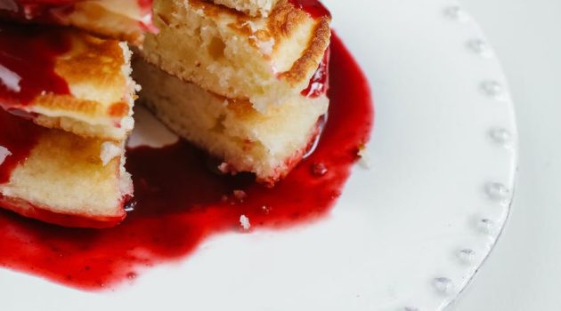 stacks of pancakes with strawberry syrup on ceramic plate