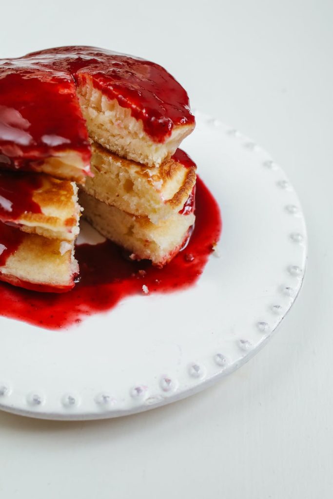 stacks of pancakes with strawberry syrup on ceramic plate