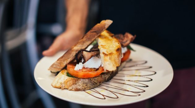 crop man demonstrating plate of appetizing grilled sandwich in restaurant