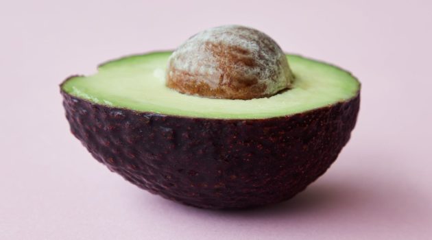 half of avocado with seed on pink surface