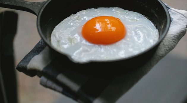 crop unrecognizable person demonstrating fried egg on pan